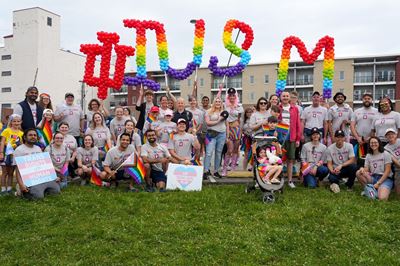 a large group photo of IU School of Medicine members at the 2022 pride parade. large balloon letters spell out IUSM in rainbow colors