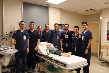 A group of PEM fellows smiling at the camera and surrounding a pediatric patient mannequin.
