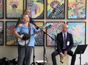 Department of Medicine Chair David Aronoff sits atop a wooden, box-like cajon drum in the lobby of the Simon Cancer Center as he plays with three other members of the band "the Crooked Finger Rhythm Review."  The band includes a banjo player and two guitar players. Colorful artwork is displayed on the wall behind the band. 