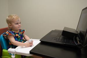 a child plays with a toy while a computer and camera in front of her conduct evaluation